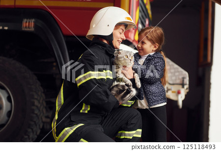 Giving beautiful scottish fold cat. Firefighter woman in uniform is with a little girl 125118493