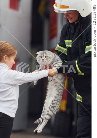 Giving scottish fold cat to the owner. Firefighter woman in uniform is with a little girl Giving scottish fold cat to the owner. Firefighter woman in uniform is with a little girl 125118499