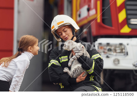 Cute scottish fold cat is in the hands. Firefighter woman in uniform is with a little girl 125118500