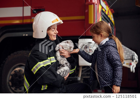 Cute scottish fold cat is in the hands. Firefighter woman in uniform is with a little girl 125118501