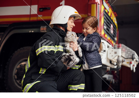 Cute scottish fold cat is in the hands. Firefighter woman in uniform is with a little girl 125118502