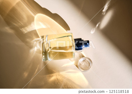 Perfume on a beige background in the rays of bright sun with beautiful highlights. 125118518