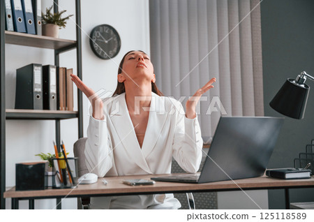 Sitting, smiling and raising hands. Young beautiful woman in formal clothes is working at office 125118589