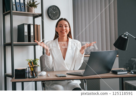 Sitting, smiling and raising hands. Young beautiful woman in formal clothes is working at office 125118591