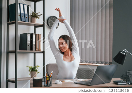 Takes a break, stretches her hands. Young beautiful woman in white clothes is in the office Takes a break, stretches her hands. Young beautiful woman in white clothes is in the office 125118626