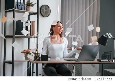 Throwing stickers up into air. Young beautiful woman in white clothes is in the office Throwing stickers up into air. Young beautiful woman in white clothes is in the office 125118633