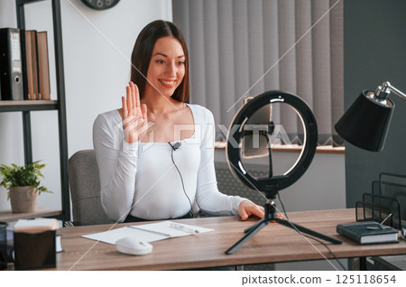 Beauty master class by using smartphone. Young beautiful woman in white clothes is in the office Beauty master class by using smartphone. Young beautiful woman in white clothes is in the office 125118654