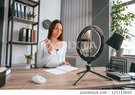 Professional lighting. Online master class. Young beautiful woman in white clothes is in the office 125118660