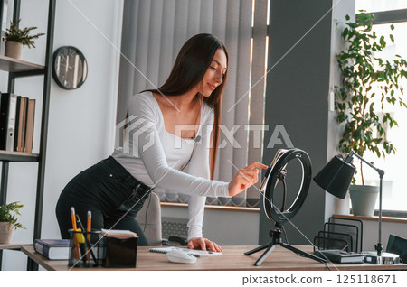 Setting up the smartphone for recording. Young beautiful woman in white clothes is in the office 125118671