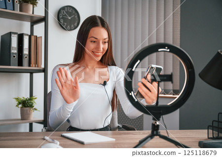 Talking, doing online master class. Young beautiful woman in white clothes is in the office 125118679