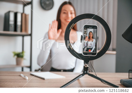 Talking, doing online master class. Young beautiful woman in white clothes is in the office 125118682