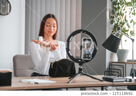 Showing cream for the skin on the camera. Young beautiful woman in white clothes is in the office Showing cream for the skin on the camera. Young beautiful woman in white clothes is in the office 125118692