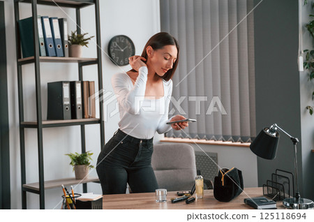 Standing and using laptop. Young beautiful woman in white clothes is in the office Standing and using laptop. Young beautiful woman in white clothes is in the office 125118694