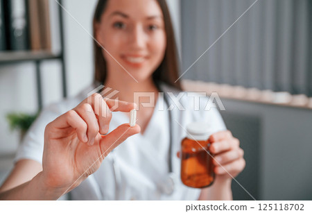 Close up view of pill that is in the hand. Young beautiful female doctor in white coat is in the office 125118702