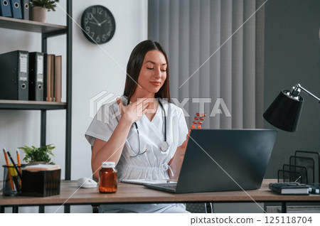 Doing online consultation. Young beautiful female doctor in white coat is in the office Doing online consultation. Young beautiful female doctor in white coat is in the office 125118704