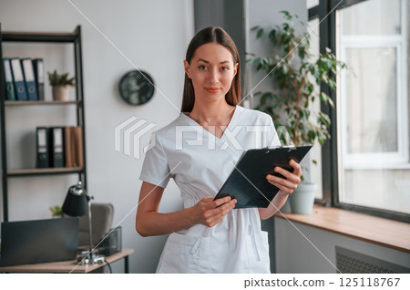 Smiling young beautiful woman in white clothes is in the office with notepad 125118767