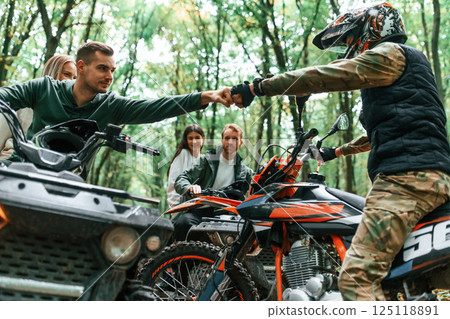 Knocking fists, gesture. Two couples on ATV with man that is on the bike in the forest Knocking fists, gesture. Two couples on ATV with man that is on the bike in the forest 125118891