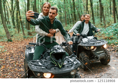 Making a selfie by smartphone. Two couples on a quad bike in the forest during the day Making a selfie by smartphone. Two couples on a quad bike in the forest during the day 125118908