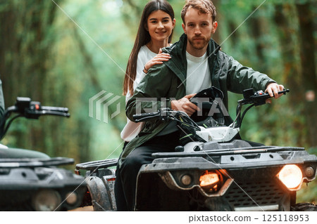 Man is handling the transport. Young couple riding a quad bike in the forest 125118953