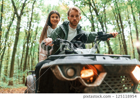Man is handling the transport. Young couple riding a quad bike in the forest Man is handling the transport. Young couple riding a quad bike in the forest 125118954