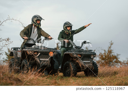 Showing the path by a hand. Two men are on the quad bikes outdoors on the field 125118967