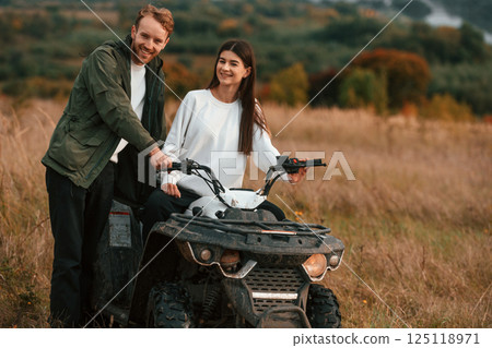 Lovely young couple is with quad bike outdoors on the field Lovely young couple is with quad bike outdoors on the field 125118971