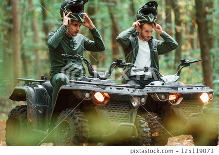 Wearing helmets. Two male atv riders is in the forest together Wearing helmets. Two male atv riders is in the forest together 125119071