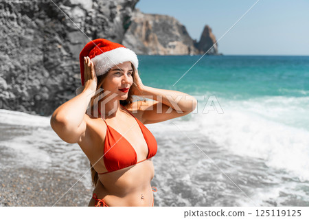 A woman in Santa hat on the seashore, dressed in a red swimsuit. New Year's celebration in a hot country A woman in Santa hat on the seashore, dressed in a red swimsuit. New Year's celebration in a hot country 125119125