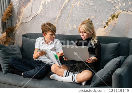 Kids Laptop Couch Learning Together: Two children working on a laptop while sitting on a couch. 125119149