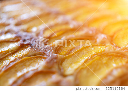 A close up of a dessert made of sliced peach. The dessert is covered in a caramel glaze and has a golden brown crust. The peach are arranged in a spiral pattern, creating a visually appealing A close up of a dessert made of sliced peach. The dessert is covered in a caramel glaze and has a golden brown crust. The peach are arranged in a spiral pattern, creating a visually appealing 125119164