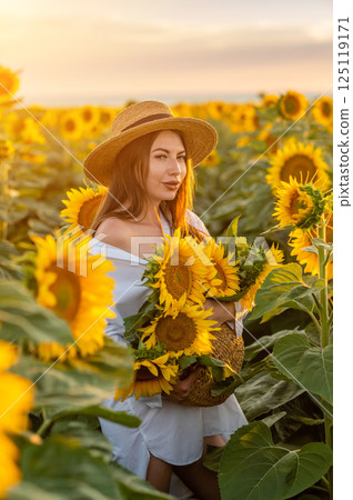 A girl in a hat on a beautiful field of sunflowers against the sky in the evening light of a summer sunset. Sunbeams through the flower field. Natural background. A girl in a hat on a beautiful field of sunflowers against the sky in the evening light of a summer sunset. Sunbeams through the flower field. Natural background. 125119171
