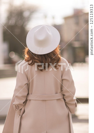 Back view of happy woman wearing hat and coat walking down street on sunny spring day. People, lifestyle, travel and vacations concept Back view of happy woman wearing hat and coat walking down street on sunny spring day. People, lifestyle, travel and vacations concept 125119313