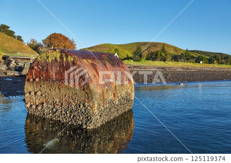 Beach campsite on an island with rusty boiler in the water 125119374