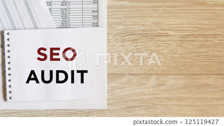 On a wooden office table there is a notebook with the text of an SEO audit and papers with reports On a wooden office table there is a notebook with the text of an SEO audit and papers with reports 125119427