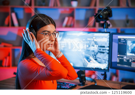 In headphones. Young beautiful game streamer is indoors with pc 125119600