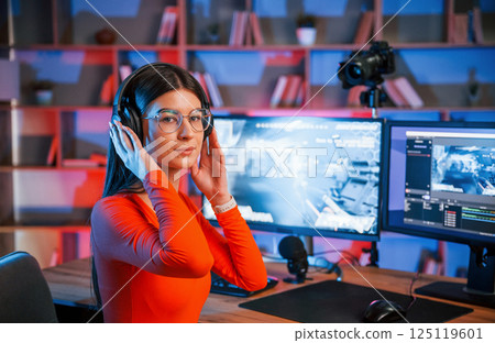 Wearing headphones. Young beautiful game streamer is indoors with pc 125119601