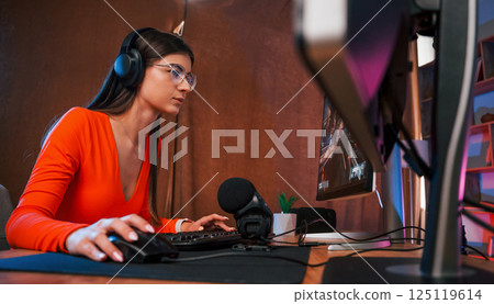 Focused on the game process. Young beautiful streamer is indoors with pc Focused on the game process. Young beautiful streamer is indoors with pc 125119614