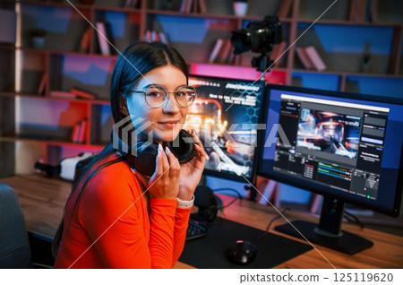 Sitting and smiling. Young beautiful game streamer is indoors with pc Sitting and smiling. Young beautiful game streamer is indoors with pc 125119620