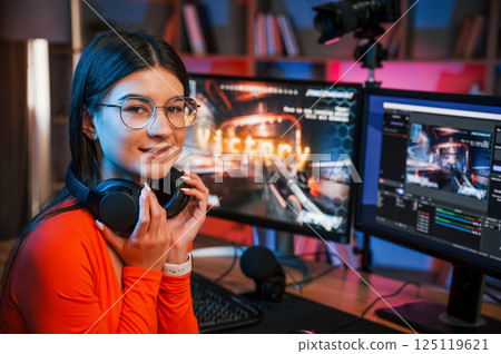 Sitting and smiling. Young beautiful game streamer is indoors with pc Sitting and smiling. Young beautiful game streamer is indoors with pc 125119621