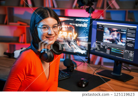 Sitting and smiling. Young beautiful game streamer is indoors with pc 125119623
