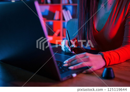 Young female retoucher working with computer and graphic tablet in neon lighting office Young female retoucher working with computer and graphic tablet in neon lighting office 125119644