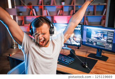 Raising hands up, celebrating the victory. Male game streamer in casual clothes is indoors with pc Raising hands up, celebrating the victory. Male game streamer in casual clothes is indoors with pc 125119669