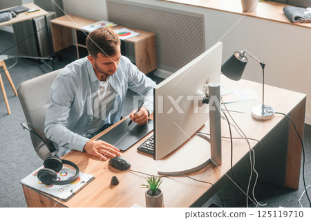 Top view. Designer is sitting by the computer and using graphics tablet with stylus 125119710