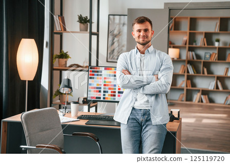 Standing against pc. Young male designer is in the modern office Standing against pc. Young male designer is in the modern office 125119720