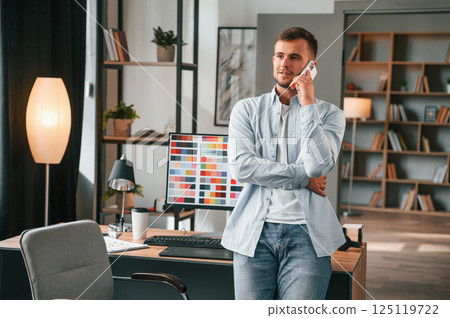 Talking by phone. Young male designer is in the modern office 125119722