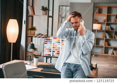 Talking by phone. Young male designer is in the modern office Talking by phone. Young male designer is in the modern office 125119725