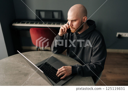 Top view of professional freelancer male working remotely, communicating on smartphone and typing on laptop, managing business while multitasking in contemporary home workspace, sitting at desk. Top view of professional freelancer male working remotely, communicating on smartphone and typing on laptop, managing business while multitasking in contemporary home workspace, sitting at desk. 125119831