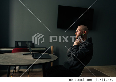 Tired freelancer touching neck while sitting at home office desk with laptop, looking pensive and contemplative after long day of work. Exhausted programmer pondering challenging project. 125119839