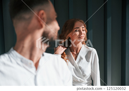 Man looking at his woman. Beautiful young couple is standing together against dark green background 125120032