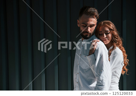 Embracing each other. Beautiful young couple is standing together against dark green background Embracing each other. Beautiful young couple is standing together against dark green background 125120033